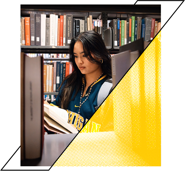 A woman in a blue shirt standing in a library, reading a book